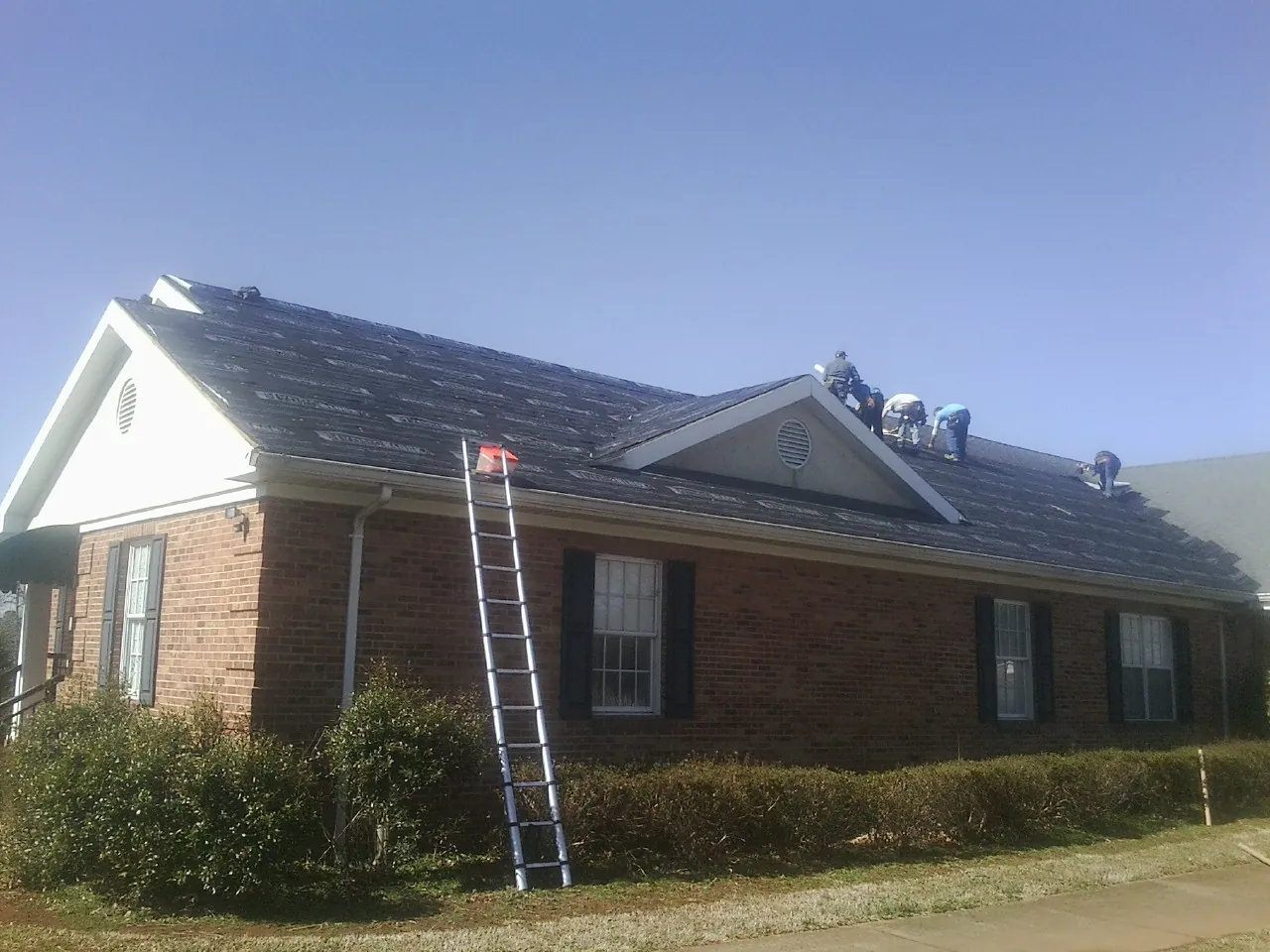 Crew tearing shingles off a brick ranch roof with a ladder set — Metal Roof Repair work by our crew in Salida