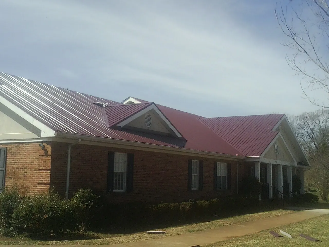 Red metal roof with gabled entries on a long brick building, from a Hail Damage Roof Repair job in Salida